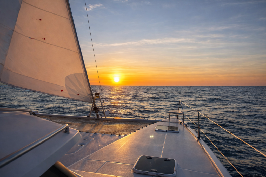 Vue depuis l’avant d’un catamaran en mer au coucher du soleil, illustrant le temps long et la préparation d’un projet de vie en mer.